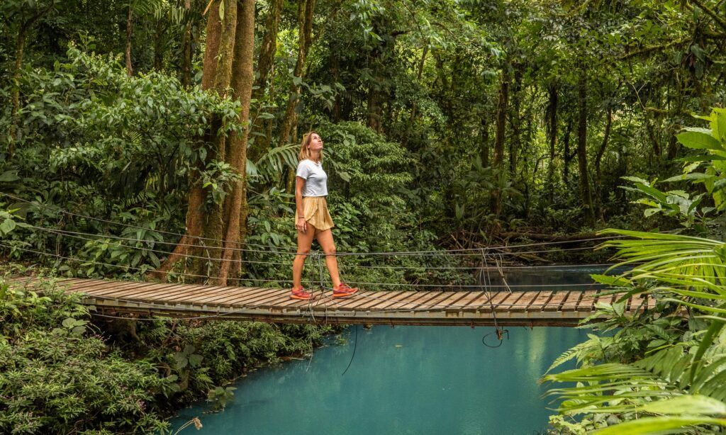 Stunning view of woman walking over rope bridge in rain forest lush greens Luxury Travel Destinations