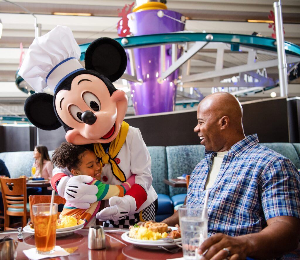 cute father and daughter eating breakfast at Disney Mickey dressing in chef outfit is hugging girl.