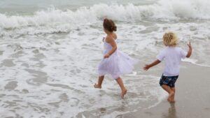 A Boy and a girl running in summer florida clothers with dress and white shirt running into St Augustine crashing wave