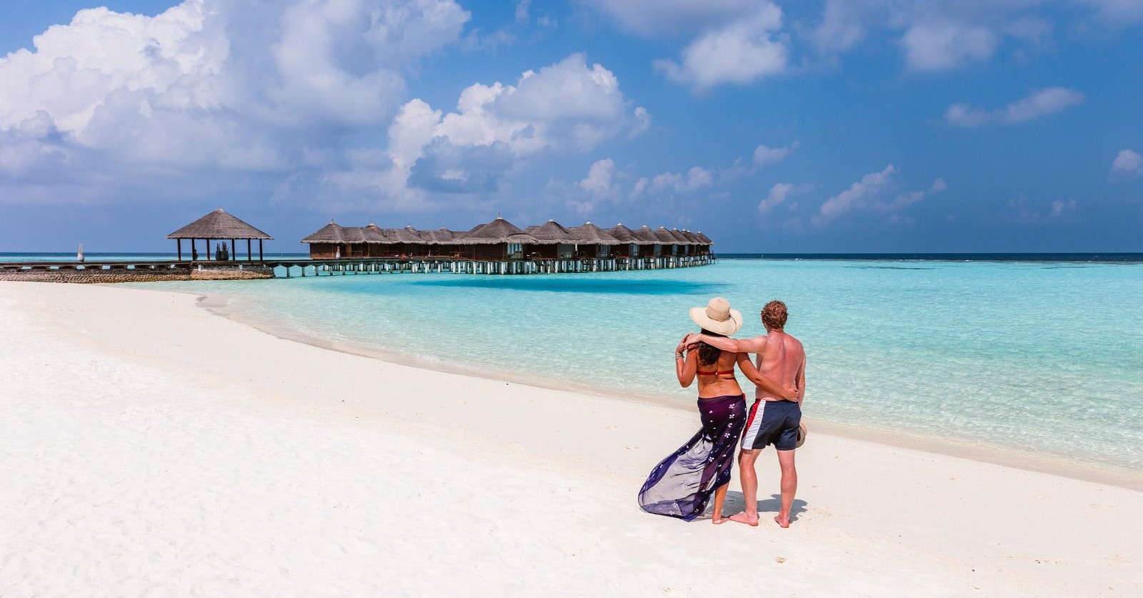 Photo of Couple on pure white sand beach looking out into the aqua blue water Luxury Travel Destinations