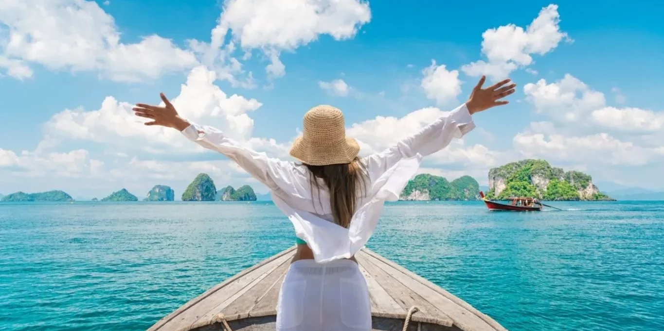 woman standing on bow of boat with arms wide open looking at the aqua water