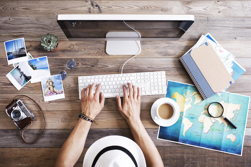 person sitting at their desk researching travel coffee cup, map laptop