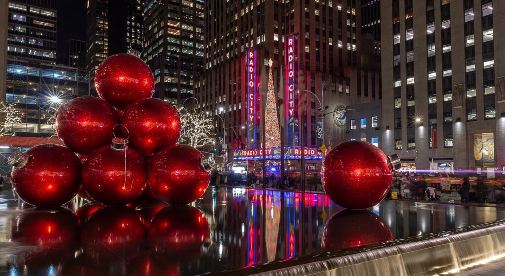 New York NY looking at Radio city musica hall with large decorative christmas balls over the fountains at night with all the city all light up decorative