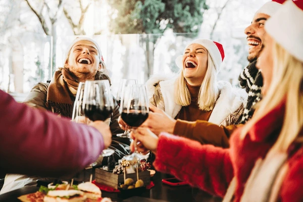 Happy family and friends sitting around a table laughing in santa outfits drivng winfe together at happy hour