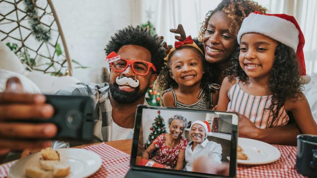 a family taking a christmas picture dressed up in sweaters by the tree and grandma and grandpa watching